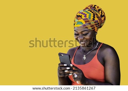 Ghana woman with African colorful headdress standing and chatting with mobile phone, illustrating the wireless technology in today's society Royalty-Free Stock Photo #2135861267