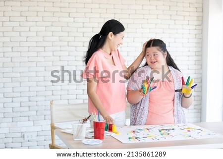 woman teacher and down syndrome girl showing painted hands for drawing a picture on paper