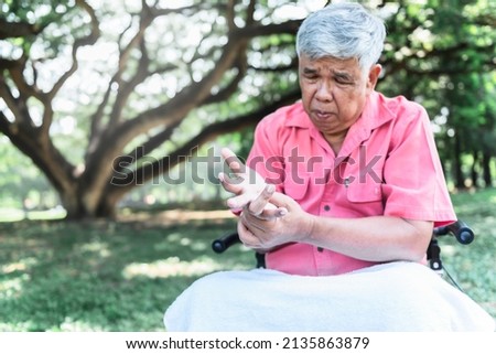 Blurred soft images of Asian elderly man, Patients wrist pain hands, due to a nervous system illness and paralysis, On blur tree in garden  background, to elderly and health care concept. Royalty-Free Stock Photo #2135863879