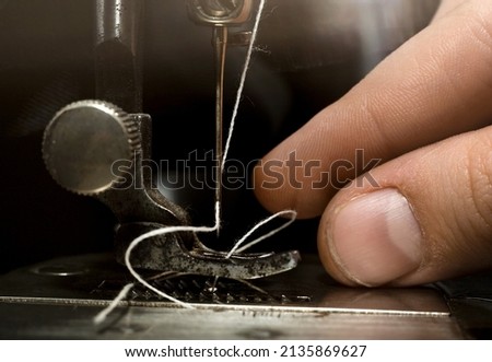 A hand threads a needle in an old retro sewing machine. Tools for the work of a tailor, fashion designer and seamstress