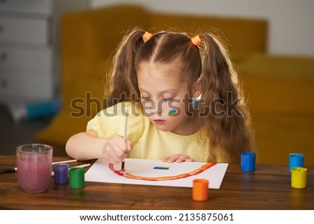 Little sad girl draws a picture about Ukraine. Draws a rainbow and the Ukrainian flag. Little artist