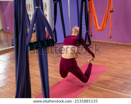 Girl leans back with help of hammock doing fly yoga exercises. Sport slim girl hanging on hammocks. Enhancing flexibility, building strength, easing sore joints or muscles