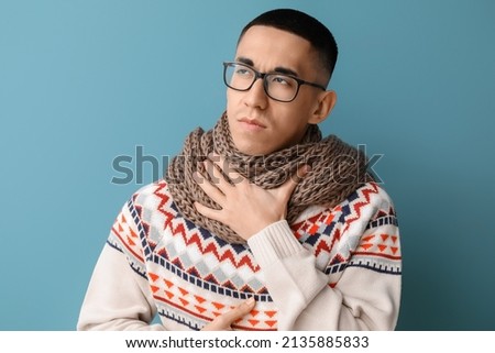 Ill Asian man with sore throat on blue background