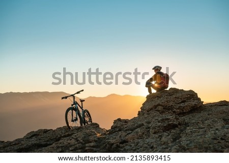 Cyclist mtb biker sits and relax on mountain top at sunset Royalty-Free Stock Photo #2135893415