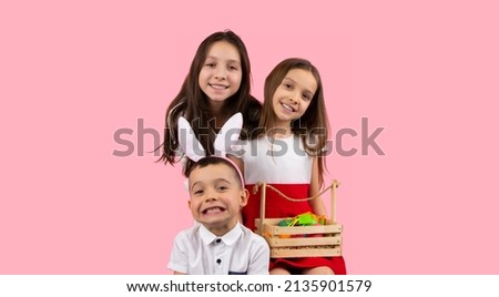 Picture of three smiling children two sisters holding basket with eggs and a boy wearing bunny ears on head, Easter concept holiday.