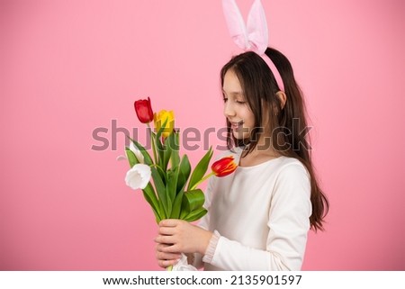 Photo of a beautiful brunette little girl wearing bunny ears on head looking at the tulips she holding in her hands.