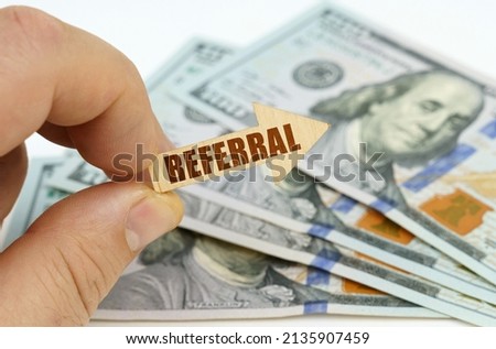 Business and finance concept. In the hands of a man is an arrow with the inscription - REFERRAL, in the background there are dollars.