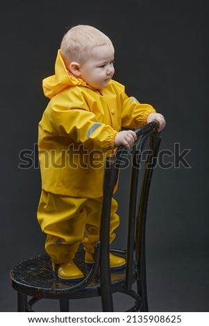 a little boy stands on chair in yellow firefighter suit