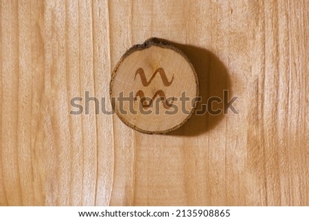 Close-up shot of a piece of wood with a zodiac sign engraved on it, especially the aquarius sign