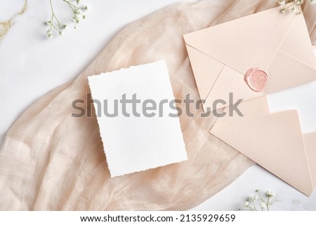 Blank white invitation card with pink envelopes and gypsophila branches. Wedding stationery set. Flat lay, top view, copy space. Royalty-Free Stock Photo #2135929659