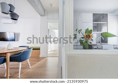 Kitchen with glass partition, circular wooden dining table, gray ceiling lamps and plant on one side