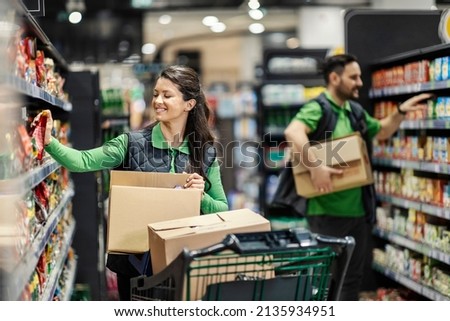 Happy employees putting products on shelves in supermarket. Royalty-Free Stock Photo #2135934951