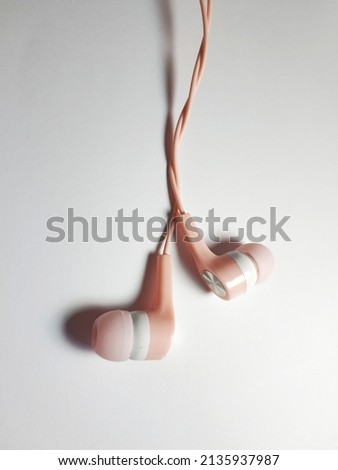 A pink and white headset or earphones with twisted wires. Isolated photo with white background and a little negative space.