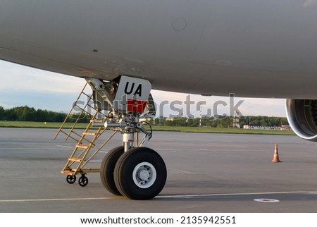 Horizontal photo with a fragment of an airplane at the airport. Yellow stairs near the aircraft landing gear. A sign with the inscription UA ​​on the hatch of the aircraft.