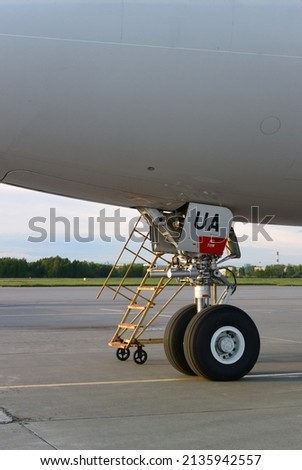 Vertical photo with a fragment of an airplane at the airport. A sign with the inscription UA ​​on the hatch of the aircraft. Yellow stairs near the aircraft landing gear.