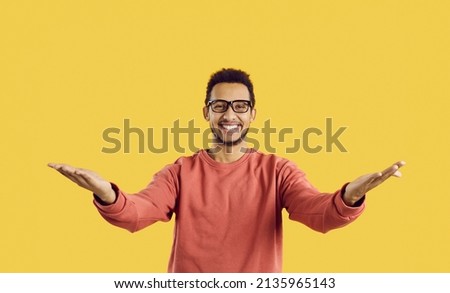 You did it. Congratulations. Happy cheerful positive young ethnic man in eyeglasses standing against yellow color background looking at camera, smiling and spreading his arms wide open for a warm hug Royalty-Free Stock Photo #2135965143