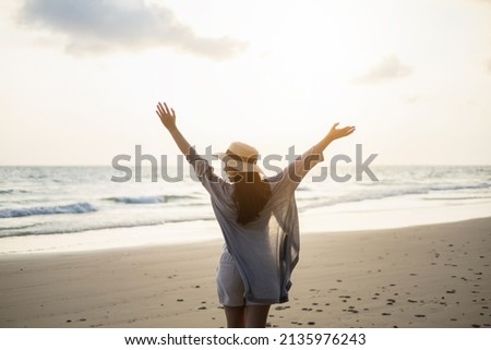 Rear view Beautiful asian woman stretching arm up into sky feeling happy at the beach with sunset. Take a break from work go on a trip. Woman travel in holiday weekend summertime. Relax vacation time
