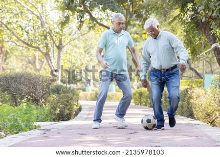 Two senior man having fun while playing football at park
