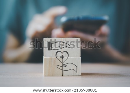 heart icon between hands on wooden cube blocks with blurred senior woman hold smartphone for online health consulting, organ donation concept