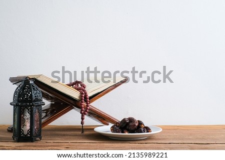 Blurred view of The Holy Al Quran with written Arabic calligraphy meaning of Al Quran and rosary beads or tasbih, Arabic word translation : The Holy Al Quran Royalty-Free Stock Photo #2135989221