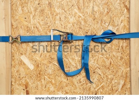 Ratchet truck cargo tie downs clasp chipboard box. Blue load belt over wooden osb surface