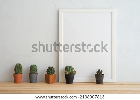 Empty white photo frame and cute cactus pots mockup on wooden table with white wall background copy space. Creative ideas, home decoration design and slow life concept