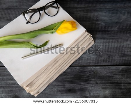 A stack of newspapers, glasses and a ballpoint pen on a wooden background.