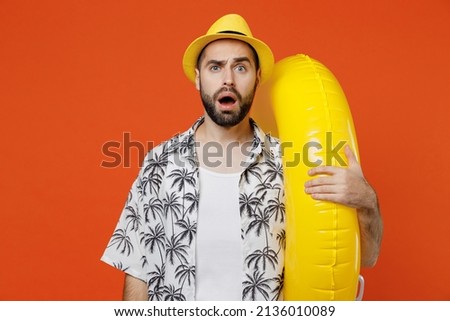 Young dissatisfied shocked tourist man wear beach shirt hat hold inflatable ring travel abroad on weekends isolated on plain orange background studio portrait. Summer vacation sea rest sun tan concept Royalty-Free Stock Photo #2136010089