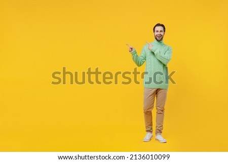 Full body smiling happy fun young man 20s wearing mint knitted sweater point index finger aside on workspace area isolated on plain yellow background studio portrait. People lifestyle fashion concept