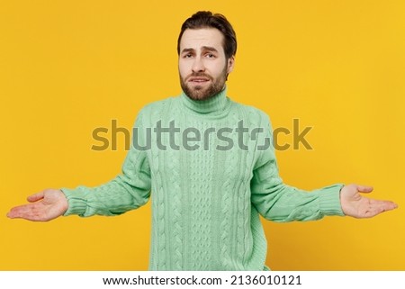 Young confused man 20s wearing mint knitted sweater spread hands shrugging shoulders looking puzzled, have no idea isolated on plain yellow background studio portrait. People lifestyle fashion concept