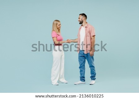 Full body side view happy young couple two friends family man woman in casual clothes hold hands folded handshake gesture together isolated on pastel plain light blue color background studio portrait Royalty-Free Stock Photo #2136010225