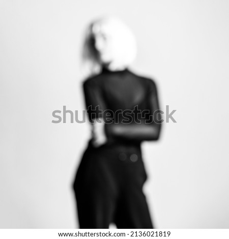 Abstract beauty and fashion concept. Black and white blurred and defocused woman silhouette image background. Woman with black outfit and white wig. Image contains noise and grain
