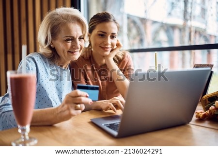 Happy mature mother using credit card and laptop with her daughter for online shopping while relaxing in a cafe. Royalty-Free Stock Photo #2136024291