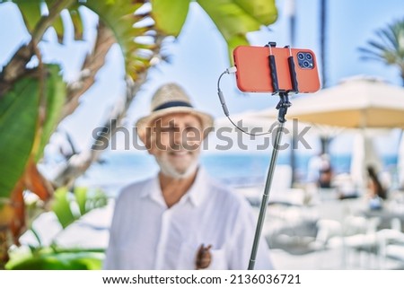 Senior man wearing summer hat making selfie by the smartphone at seaside