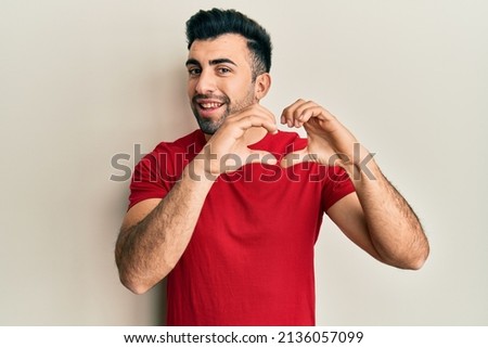 Young hispanic man wearing casual clothes smiling in love doing heart symbol shape with hands. romantic concept. 