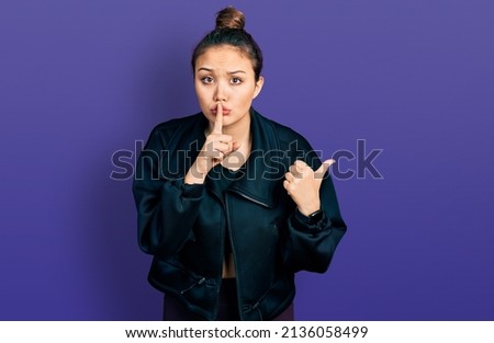 Young hispanic girl wearing sportswear asking to be quiet with finger on lips pointing with hand to the side. silence and secret concept. 