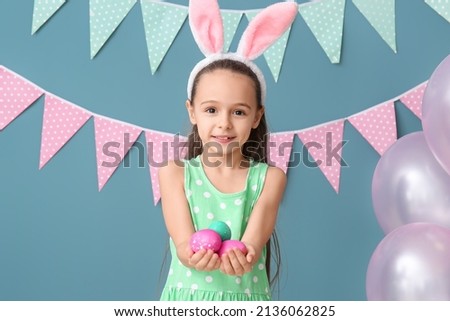 Little girl with bunny ears holding Easter eggs on blue background