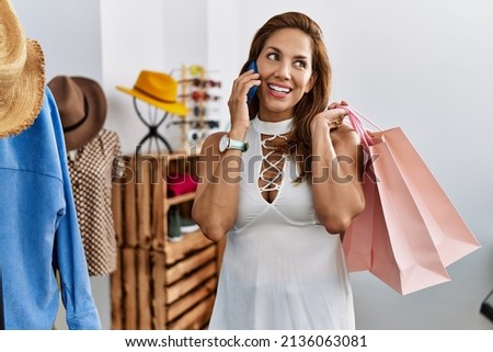 Young latin woman customer shopping talking on the smartphone at clothing store