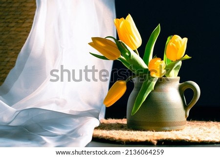 Still life with bouquet of yellow tulip flowers in old vintage jug, in beam of light on dark background.Art photography.