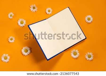 Navy blue notepad with white sheets and white daisies on summer orange background. Plans for summer to do list
