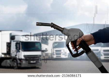A hand with a fuel nozzle on the background of trucks. The concept of a fuel crisis due to rising prices. Royalty-Free Stock Photo #2136086171