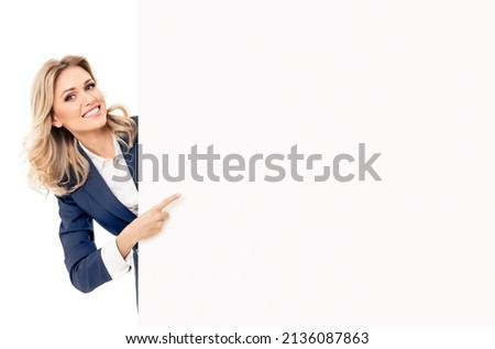 Happy smiling blond young business woman in blue suit, standing behind, peeping from blank banner or mock up signboard billboard bill board, showing copy space isolated over white background. big save