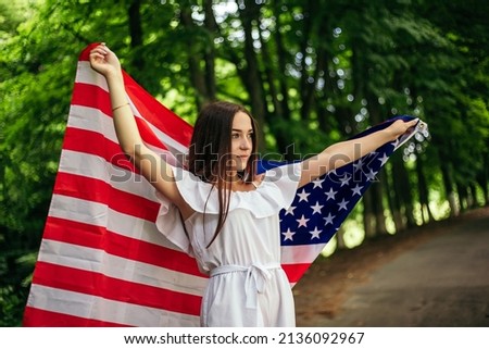 Happy 4th of July! Independence Day celebrating. Patriotic woman hold wrapped in american national flag waving on wind and walking on the road. Stars and stripes. Freedom concept.
