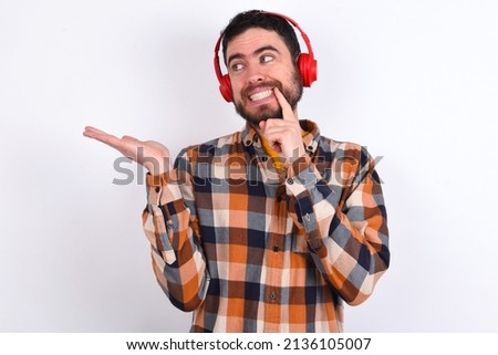 Positive young caucasian man wearing plaid shirt over white background advert promo touches teeth with finger.