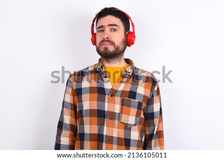 Displeased young caucasian man wearing plaid shirt over white background frowns face feels unhappy has some problems. Negative emotions and feelings concept