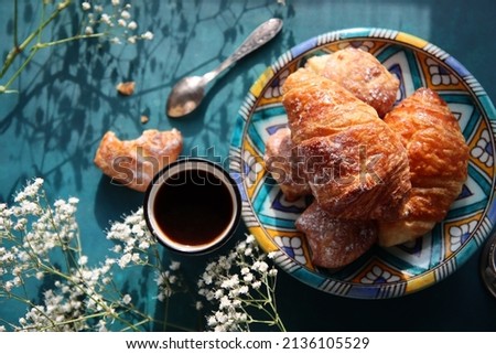 Freshly baked croissants, black coffee and gypsophila flowers on deep blue background. Beautiful morning photo. Food still life picture. 