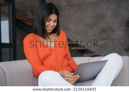 Portrait of smiling woman using laptop computer watching training courses sitting on sofa. Copywriter typing working freelance project from home. Beautiful female shopping online 