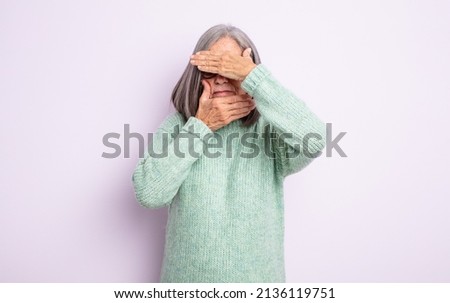 senior pretty woman covering face with both hands saying no to the camera! refusing pictures or forbidding photos