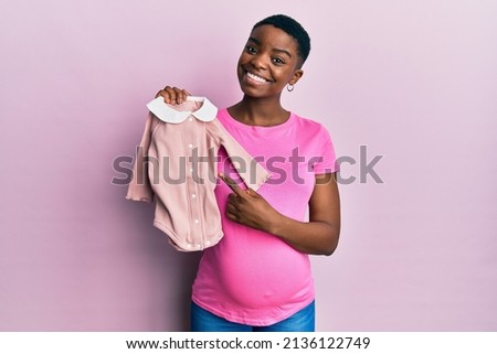 Young african american woman expecting a baby holding clothes smiling happy pointing with hand and finger 