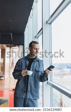 European male freelancer in checking notification on smartphone about money transactions, doing business online, working remotely while in cafe and drinking coffee